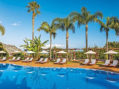 Pool mit blauer Wasseroberfläche, Sonnenliegen und Palmen unter klarem Himmel in einem Hotelresort.