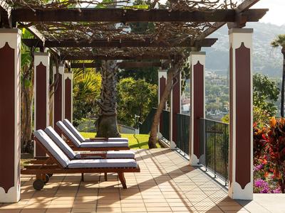 Terrasse mit Liegestühlen unter einer Pergola, Blick auf Garten und Landschaft.