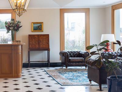 Eleganter Hotellobby mit Holztheke, Ledersessel und großen Fenstern.