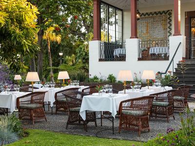 Außenbereich eines Hotels mit gedeckten Tischen und geflochtenen Stühlen in einem Garten.