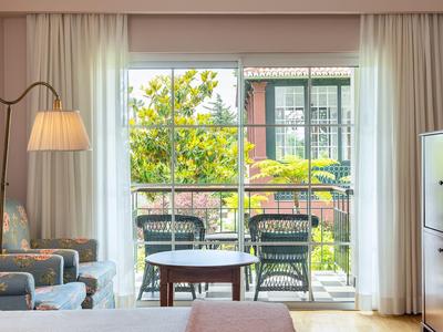 Wohnzimmer mit Sesseln und Blick auf Balkon mit Gartenmöbeln und grünem Gartenlicht.
