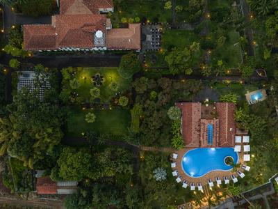 Luftaufnahme eines Hotelkomplexes mit Pool, Liegestühlen und dicht bewaldetem Garten.