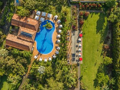 Luftaufnahme eines Hotels mit geschwungenem Pool, umgeben von Sonnenschirmen und Gartenanlagen.