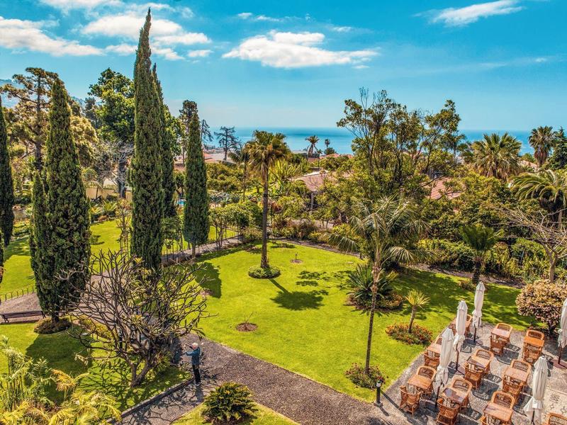 Giardino verde con cipressi snelli, palme e zona salotto in località costiera soleggiata.