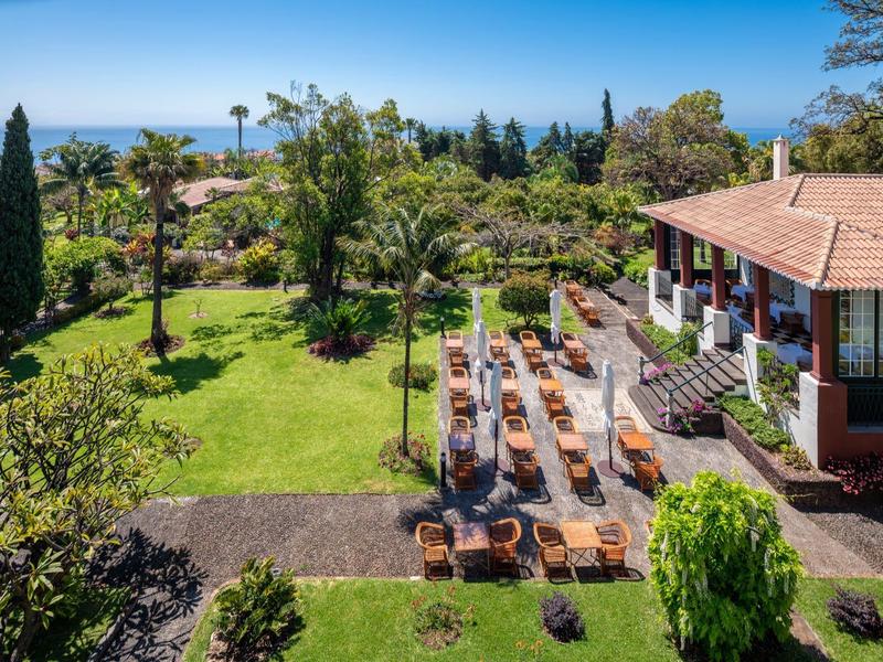 Giardino dell'hotel con lettini, alberi verdi e vista mare sotto un cielo limpido.