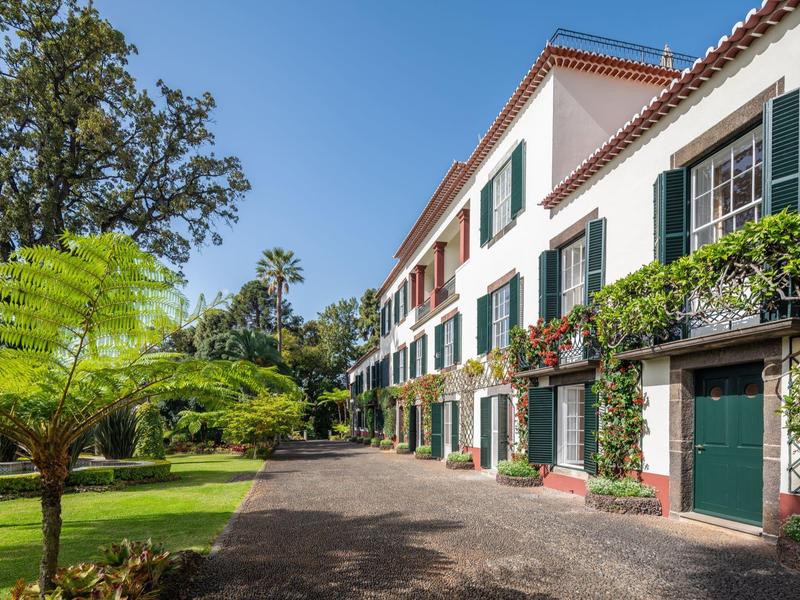 Edificio dell'hotel su più piani con persiane verdi e vegetazione rigogliosa nel giardino