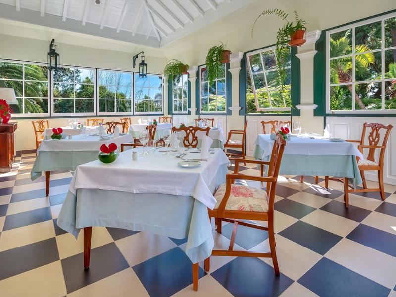 Sala da pranzo luminosa con pavimento a scacchiera, tavoli con tovaglie bianche e sedie di legno.