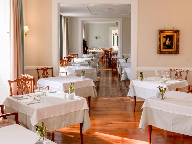 Ristorante luminoso con tovaglie bianche, pavimento in legno e arredi classici.