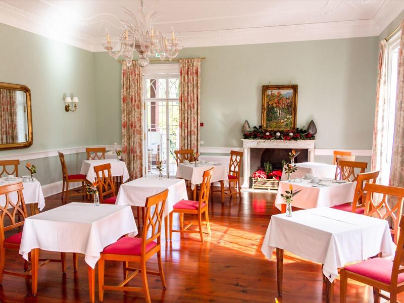 Ristorante luminoso con pavimento in legno, tovaglie bianche e grandi finestre con tende decorate.