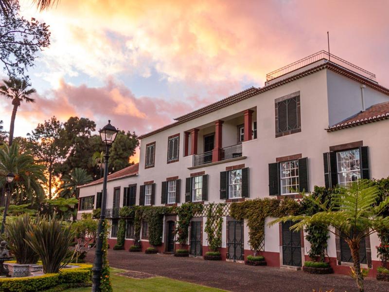 Grande edificio bianco con persiane e giardino al tramonto.