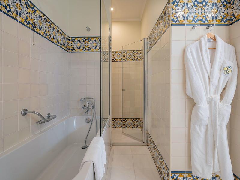 Bagno bianco con vasca, piastrelle decorative e un accappatoio bianco appeso al muro.