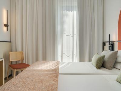 Helles Hotelzimmer mit Doppelbett, Vorhängen und minimalistischem Design.