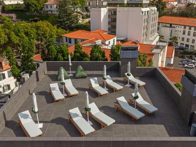 Terrasse sur le toit avec parasols et chaises longues, entourée de bâtiments et d'arbres.