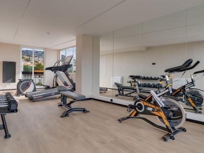 Salle de sport moderne avec vélos, tapis roulant et poids devant un grand miroir.
