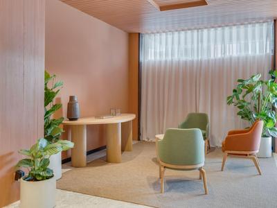 Salle d'attente moderne avec des chaises, des tables et de grandes plantes près d'une fenêtre avec des rideaux.