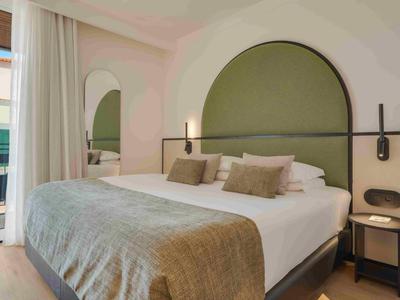 Chambre moderne avec grand lit, tête de lit ronde et balcon en arrière-plan