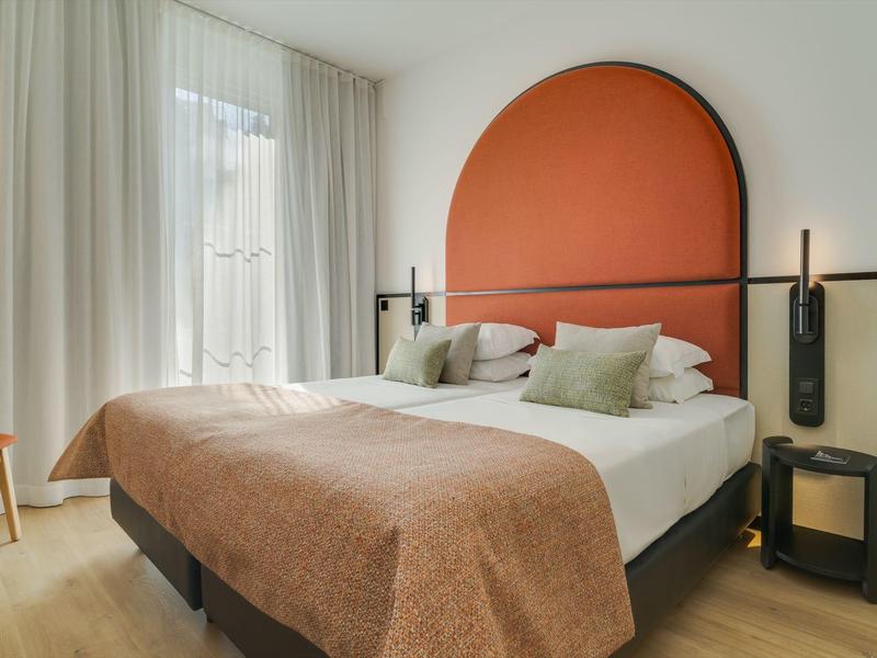 Modernes Hotelzimmer mit großem Bett, orangefarbenem Kopfteil und natürlichem Licht