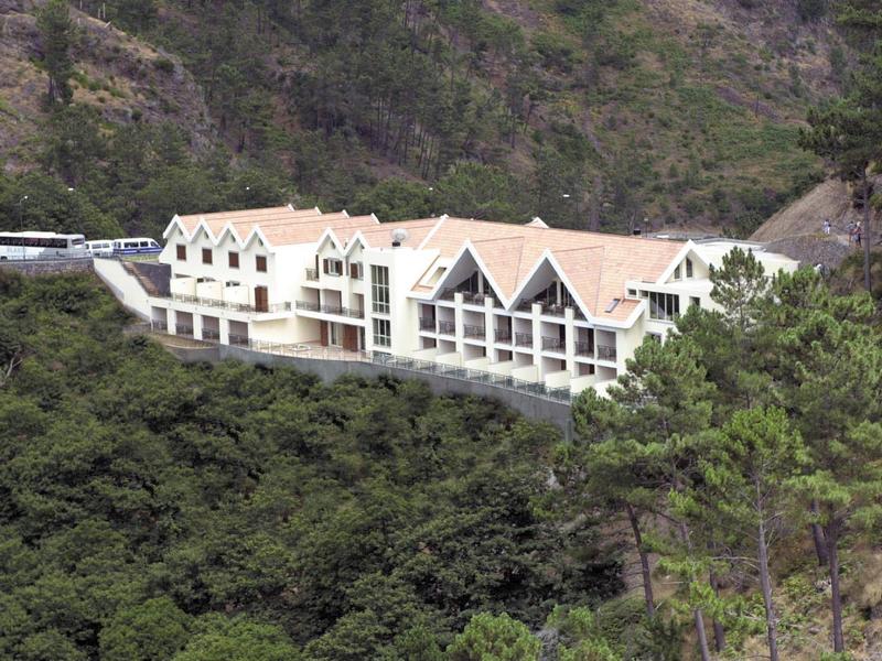 Large hotel with pointed roofs surrounded by mountains and dense green vegetation.