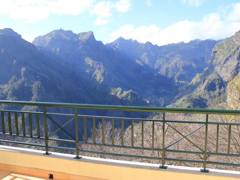 Mountain view from a balcony with metal railing on a sunny day.