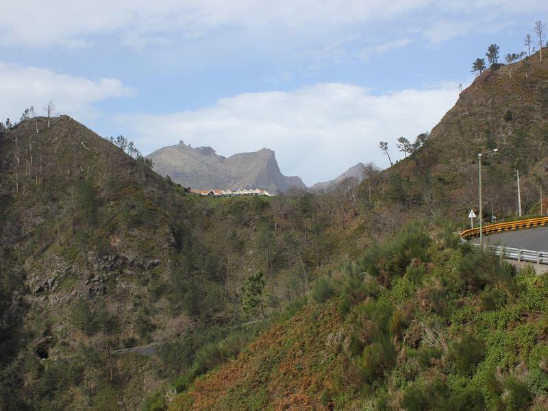Mountainous landscape with winding road and vegetation under blue sky.