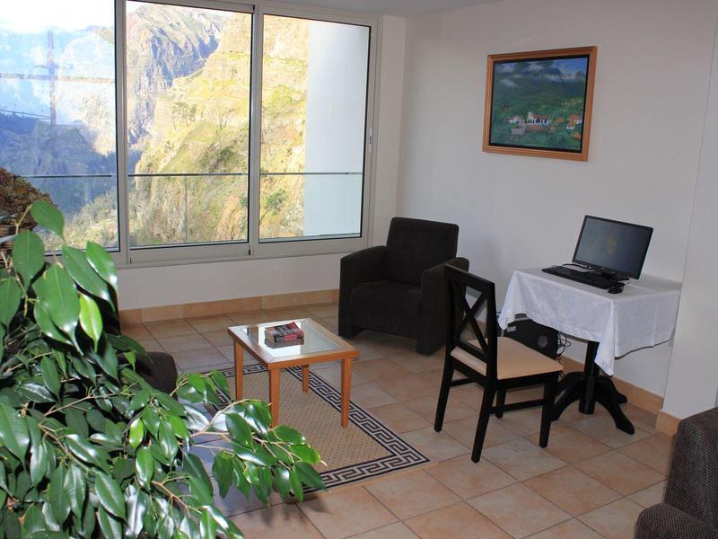 Bright living room with window and mountain view, armchair, table with laptop, and plants.