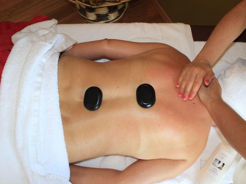 Person lies face down, receiving hot stone back massage at spa.