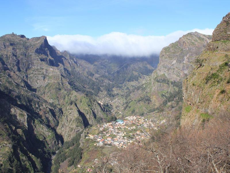 Mountain valley with a small village in the valley floor under blue sky and clouds on the horizon