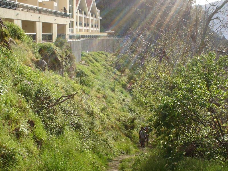 A path runs along a grassy hillside with gabled roof houses above.