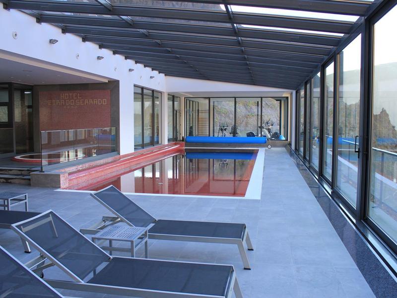 Modern indoor pool with glass walls and sun loungers in a hotel setting.