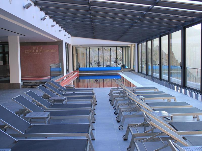 Indoor pool area with sun loungers and glass walls, modern relaxation space.