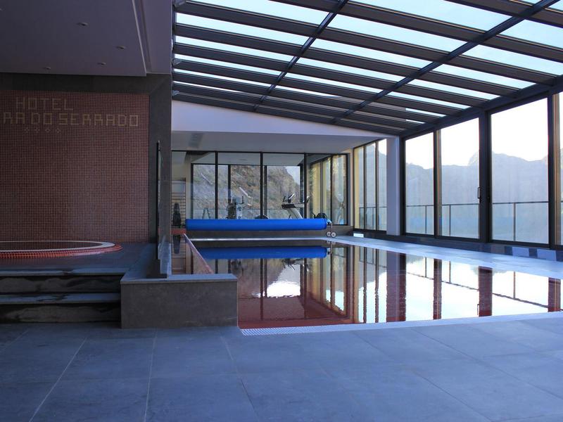 Modern indoor pool with floor-level pool cover and panoramic windows in a hotel.
