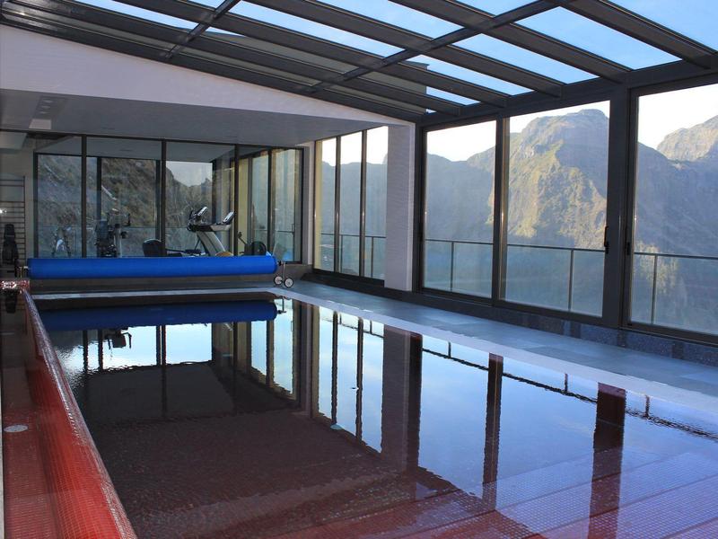 Indoor heated pool with glass walls and mountain view.