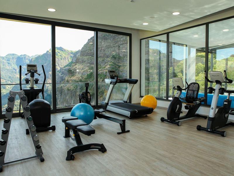 Modern gym with equipment and panoramic mountain views through large windows.