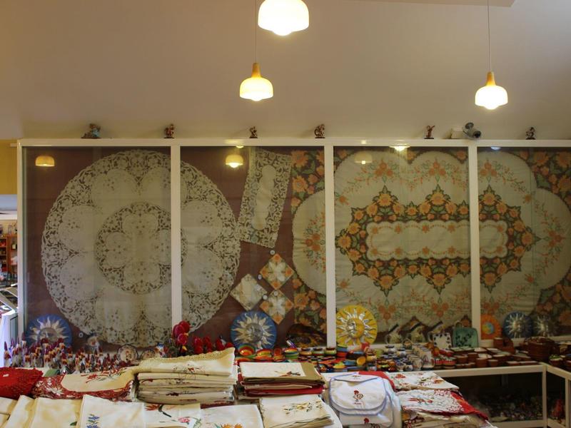 Market stall with several large colorful rugs on the wall and fabrics on the table.