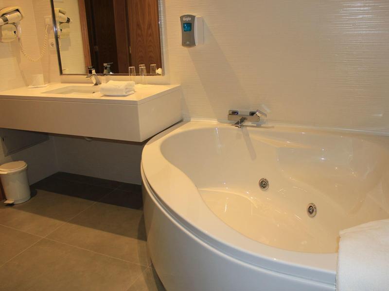 White corner bathroom with large bathtub and sink in hotel room.