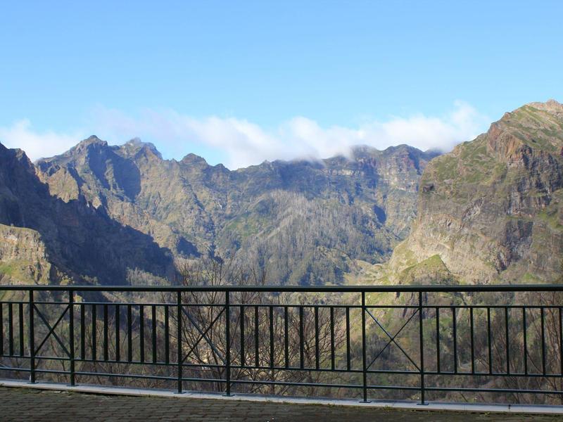 Mountain landscape with cloudy sky, viewed from a balcony with metal railing.