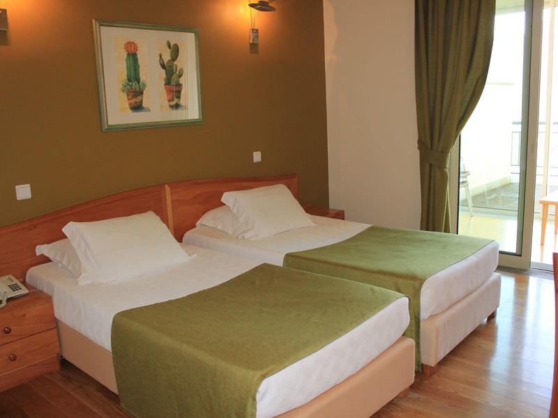 Hotel room with two beds, green blankets, and balcony with green curtains.