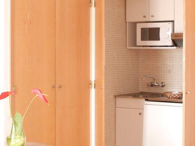 Offene Holztür zeigt kleine Hotelküche mit Mikrowelle, Spüle und Minibar neben einem Tisch mit Blume.