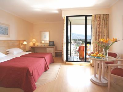 Hotelzimmer mit zwei Doppelbetten, hellen Wänden, TV und Balkon mit Bergblick.