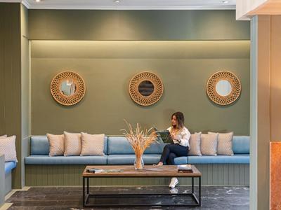 Moderne Hotellobby mit Sitzbank, Kissen, drei Wanddekorationen und einer Frau mit Laptop.