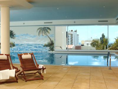 Modern binnenzwembad met ligstoelen en panoramische ramen met uitzicht op zee.