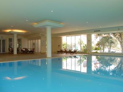 Licht binnenzwembad met grote ramen en pilaren, omgeven door planten.