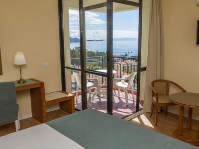 Hotelkamer met balkon en zeezicht, met tafel, stoelen en bureau.