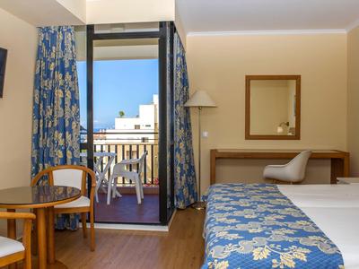 Hotelkamer met twee bedden, zithoek en balkon met uitzicht op gebouwen.