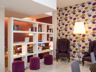 Gezellig hotel-loungedeel met boekenplank, kleurrijke krukjes en gestoffeerde fauteuils.