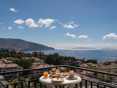 Balkon met ontbijttafel met uitzicht op stad en zee onder een blauwe lucht.