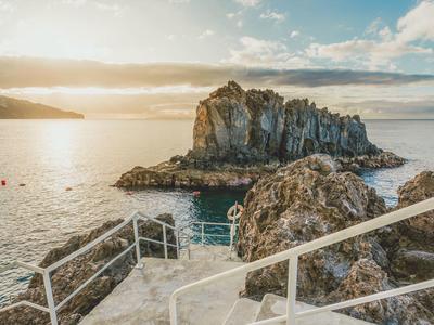 Felsige Insel im Meer mit Treppe und Geländer im Vordergrund bei Sonnenuntergang.
