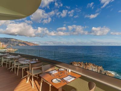 Offenes Restaurant mit Holzboden und Blick auf das blaue Meer und bewölkten Himmel.