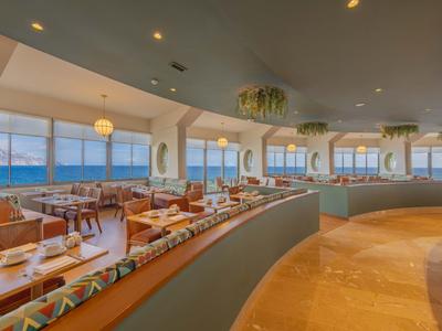 Helles Restaurant mit großen Fenstern, dekorativen Lampen und gemütlichen Sitzbereichen am Meer.