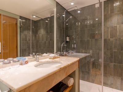 Modernes Badezimmer mit großer Holzablage, Doppelwaschbecken und Glasdusche mit dunklen Fliesen.
